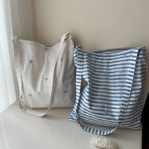 Détail de sacs cabas en coton rayés avec d'élégantes broderies de rubans bleus