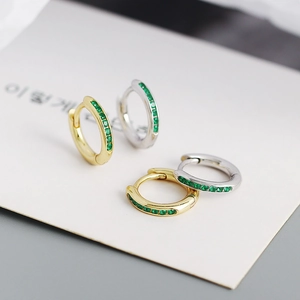 Macro shot of gold and silver S925 huggie earrings with pave-set green zircon gemstones