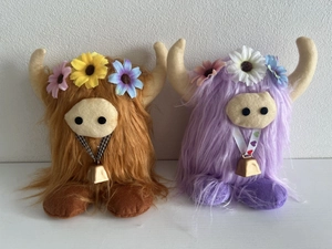 Detail of plush Highland cows with colorful flower crowns and bell collars on white base