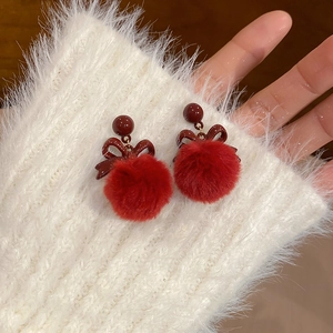 Primo piano di orecchini con fiocco e pompon rossi su una manica di maglione bianco