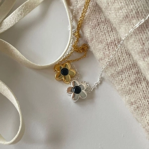 Close-up of gold and silver flower pendant necklaces with black zircon stones on soft silk