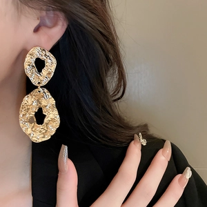 Close-up of model wearing chunky golden geometric earrings with hammered metal texture