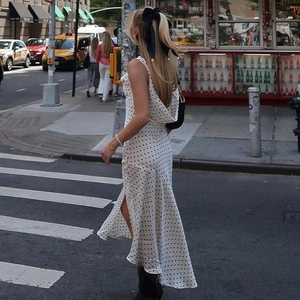 Detailed back view of white polka dot cowl neck maxi dress with side slit on city street