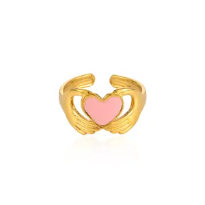 Detail of pink enamel heart ring with gold-plated hands design and adjustable band