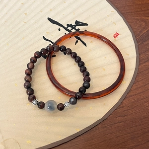 Détail du bracelet en œil de tigre rouge et jonc ambré sur un éventail traditionnel