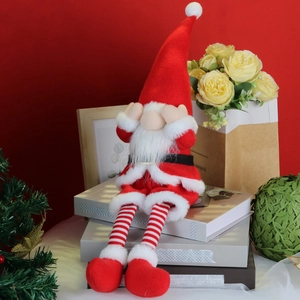 Plush Christmas gnome with long striped legs sitting on books in a red festive setting