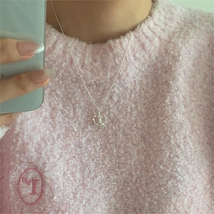 Detail of silver heart planet pendant necklace worn on pink textured sweater