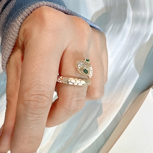 Detail of adjustable brass snake ring with white enamel scales and green gemstone eyes
