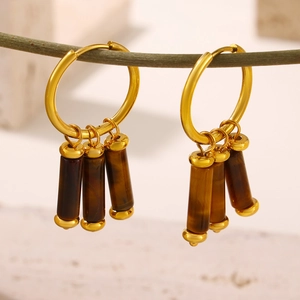 Gold hoop earrings with three tiger eye stone cylinders hanging on a wooden branch