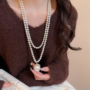 Close-up of double-layer pearl necklace with a large pendant on a soft brown sweater