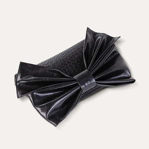 Detail of black woven evening clutch featuring a large faux leather bow and zipper