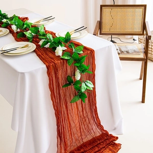 Detail of terracotta crinkled cheesecloth table runner and white rose garland on a dining table