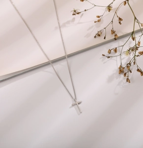 Macro detail of silver cross pendant with minimalist link chain on a clean background