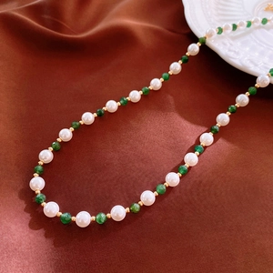Close-up of vintage pearl and green stone necklace on dark silk with ceramic plate