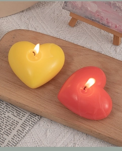 Close-up of yellow and red heart-shaped candles burning on a wooden tray with lace