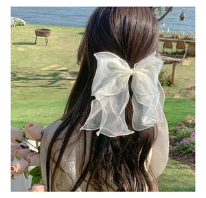 Detail of a large white layered mesh bow clip worn on long wavy hair in outdoor setting