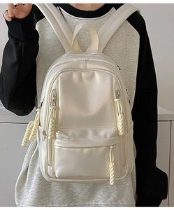 Detail of a beige satin backpack with woven zipper pulls and multiple zipper pockets