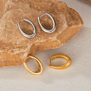 Polished stainless steel oval hoop earrings in gold and silver finish on a stone