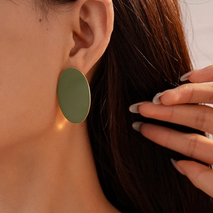 Close-up of a matte olive green oval earring with gold trim worn by a fashion model