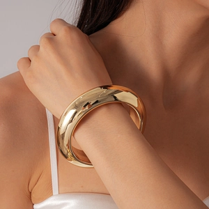 Close-up of a bold gold-finished geometric metal cuff bracelet worn by a model