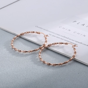 Macro detail of rose gold bamboo-textured hoop earrings on a minimalist background