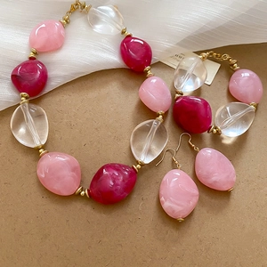 Detail of pink acrylic bead necklace, bracelet, and earring set on white fabric