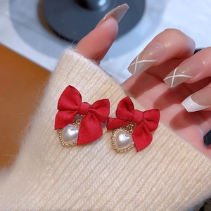 Detail showing red bow earrings with pearl heart pendants worn by a model