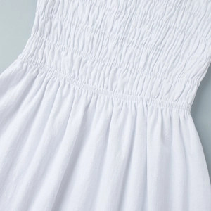 Detailed close-up of smocked bodice and elastic pleated waist on a white cotton dress