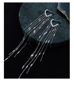Detail shot of elegant silver-colored heart-shaped long tassel earrings on a marble plate