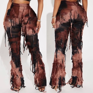 Dettaglio dei pantaloni a zampa a vita alta con motivi tie-dye e lunghe nappe a frange
