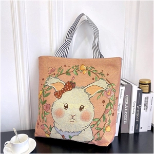 Detailed embroidered floral and rabbit patterns on a woven canvas tote bag next to coffee
