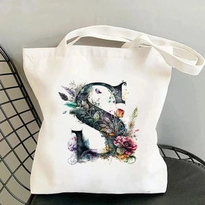 Detail of artistic floral letter S print on cream canvas tote bag resting on a chair