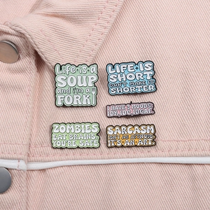 Close-up of five colorful enamel pins on a pink denim jacket with funny English phrases