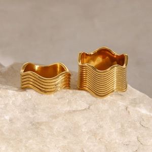 Polished gold wide wave stainless steel rings layered on a natural stone surface