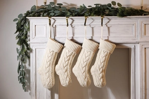 Set of 4 cream white cable knit Christmas stockings hanging on a vintage fireplace mantel