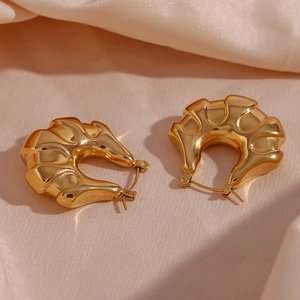 Macro view of 18K gold plated thick wavy hoop earrings on soft beige silk fabric