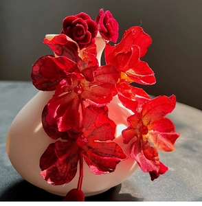 Macro detail of red fabric rose earrings with central bead on white ceramic vase
