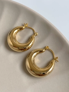 Close-up of chunky gold-toned teardrop hoop earrings on a textured ceramic tray