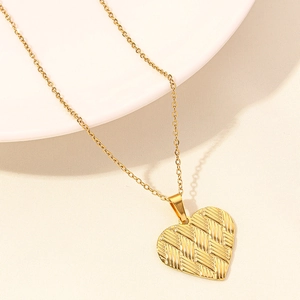 Macro shot of gold heart pendant with woven texture on a white plate with soft lighting