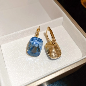 Close-up of rectangular blue gemstone earrings with gold finish in white jewelry box