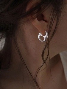 Artistic organic shaped silver earrings with a metallic luster on a female model's ear