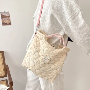 Sac bandoulière en toile matelassée beige avec sangle rose porté par un mannequin en salle