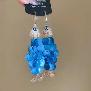 Close-up of golden fish earrings with blue shell scales and evil eye detail
