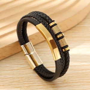 Macro detail of men's layered black woven leather bracelet with golden metal clasp and charms