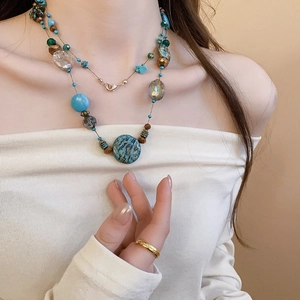 Detail of layered beaded necklace with blue faux stone pendant on a white collar