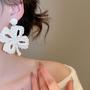 Detail shot of a model wearing cream raffia woven flower earrings with stud tops