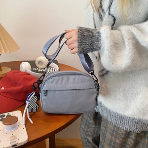 Detail of grey-blue nylon crossbody bag with adjustable strap and checkered charm