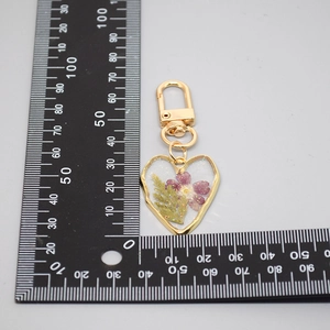 Macro shot of heart-shaped resin keychain with dried purple flowers and ruler for scale