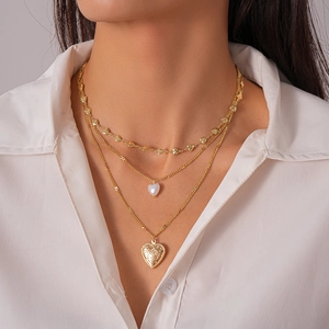 Detailed close-up of triple-layered golden necklace with heart pearl and rose relief pendant