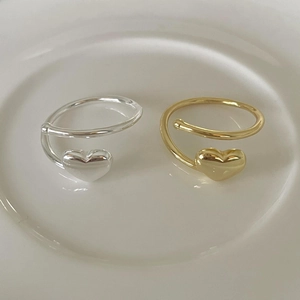Detail of minimalist silver and gold heart open rings on a clean white ceramic tray